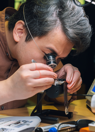 Participant using a watchmaker's loupe and precision tools while working on a mechanical wristwatch at The Watch Academy.
