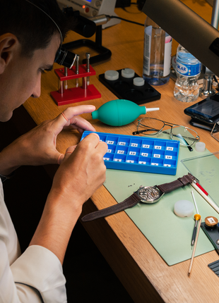Participant working at a watchmaking station equipped with precision tools, movement components and instructional materials.